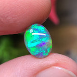 A bright green black crystal opal gemstone held in a person's hand, with a black crystal-like appearance and a play of color.