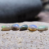 Five opal stones arranged in a row on a textured surface with a blurred background