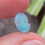 Opal stone held between fingers with a blurred natural background