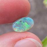 Opal stone held between fingers with a blurred natural background