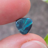 Blue gemstone held between fingers with a blurred natural background