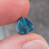 Blue gemstone held between fingers against a blurred background