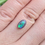 Opal stone on a person's finger with a blurred green background