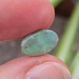 Green stone held between fingers with a blurred natural background