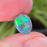 Opal stone held between fingers with a blurred green plant background