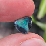 Person holding a small, multicolored stone between their fingers with a blurred natural background.
