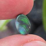 Opal stone held between fingers with a blurred natural background