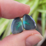 Free form shaped opals with green play of colour held between fingers against a blurred natural background