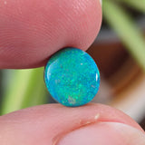 Opal stone held between fingers with a blurred natural background