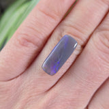 Purple gemstone held between fingers against a blurred natural background