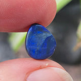 Blue stone held between fingers with a blurred natural background