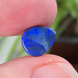Blue stone held between fingers with a blurred plant background