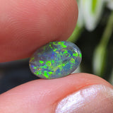 Opal stone held between fingers with a blurred natural background