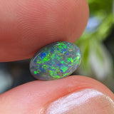 Opal stone held between fingers with a blurred natural background