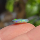 Opal stone held between fingers with a blurred natural background