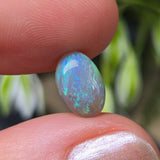 Opal stone held between fingers with a blurred natural background