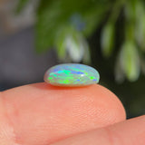 Opal stone held between fingers with a blurred natural background
