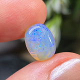 Opal stone held between two fingers with a blurred natural background