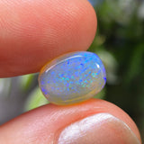 Opal stone held between fingers with a blurred natural background