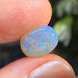 Opal stone held between fingers with a blurred natural background