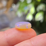 Opal stone held between fingers with a blurred natural background