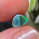 Opal stone held between fingers with a blurred natural background
