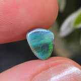 Opal stone held between fingers with a blurred natural background