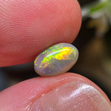 Opal stone held between two fingers with a blurred natural background