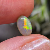 Opal stone held between two fingers with a blurred natural background