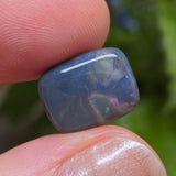 Opal stone held between fingers with a blurred green background