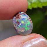 Opal stone held between fingers with a blurred green leaf background