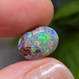 Opal stone held between fingers with a blurred green background