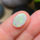 Opal stone held between fingers with a blurred natural background