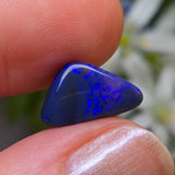 Blue opal stone held between fingers with a blurred natural background