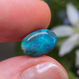 Blue opal stone held between two fingers with a blurred natural background