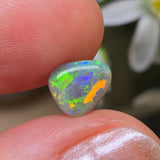 Opal stone held between fingers with a blurred natural background