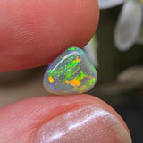 Opal stone held between fingers with a blurred natural background