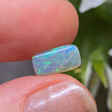 Opal stone held between fingers with a blurred natural background