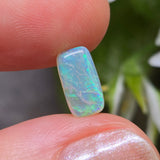 Opal stone held between fingers with a blurred natural background