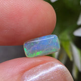 Opal stone held between fingers with a blurred floral background