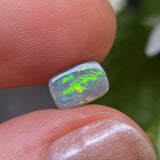 Opal stone held between fingers with a blurred natural background