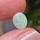 Opal stone held between two fingers with a blurred natural background