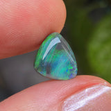 Opal stone held between fingers with a blurred green background