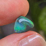 Opal stone held between fingers with a blurred green leafy background
