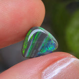 Opal stone held between fingers with a blurred green leafy background