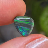 Opal stone held between fingers with a blurred green background