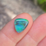 Multicolored gemstone held between fingers against a blurred natural background