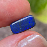 Blue opal stone held between fingers with a blurred natural background