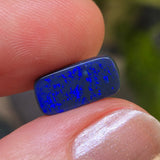 Blue speckled object held between fingers with a blurred green background