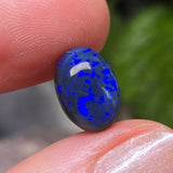 Blue opal stone held between fingers with a blurred green background